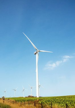 Rüzgar türbinleri, yenilenebilir yeşil enerji üretimi için güzel doğa manzarasında mavi gökyüzüne karşı tarım jeneratörleri üretiyor. Çevreye dost sanayi. Sürdürülebilir geliştirme teknolojisi kavramı.