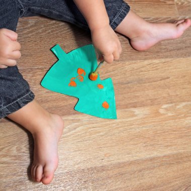 Ayak ve kolları beyaz Noel ve yeni yıl bir ev yapımı kağıt Noel ağacına bir fırça ile boya ve kırmızı dekorasyon top çizmek için bekleyen evlat. Küçük çocuk bir Hediyelik Noel için hazırlanıyor. Avrupa'nın aile gelenekleri.