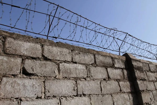 Barbed wire on top of the brick wall restricts the freedom of movement of people and protects the inviolability of private property.