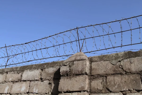 Barbed wire on top of the brick wall restricts the freedom of movement of people and protects the inviolability of private property. — Stock Photo, Image