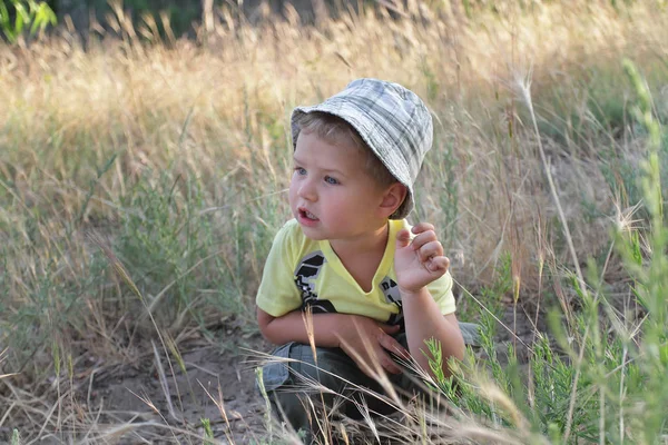 The kid in the hat sits in the field listening attentively to th