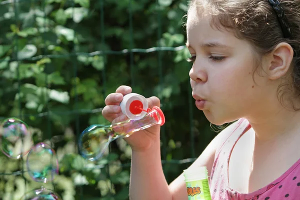 A teenage girl in a pink T-shirt concentrates blows soap bubbles. Soap bubbles as a model of the world economy — Stock Photo, Image