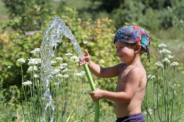 Küçük çocuk bir su hortumu ile bir sıcak yaz gününde oynuyor. Bir çocuk açık su ile oynuyor. Su kaynaklarının makul kullanım. — Stok fotoğraf