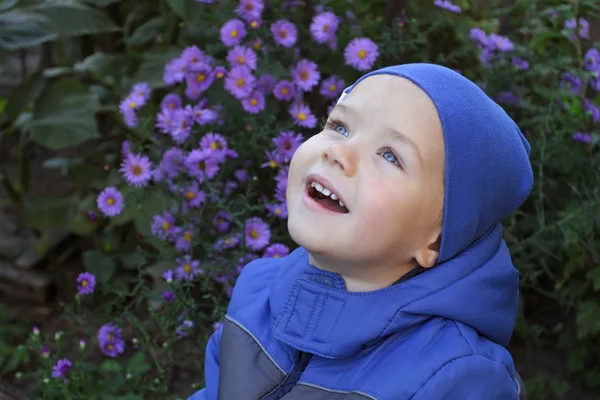 A little boy in blue demi-season clothes is emotionally laughing looking up at the sky. A kid in a blue autumn jacket and hat looks dreamily and joyfully upwards into the future. Children's dreams in the fall are particularly joyful. — Stock Photo, Image