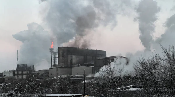 Panorama of an industrial complex with a large torch of burning gas from a pipe and huge smoke all over the sky. Pollution of the environment by factories with obsolete technologies and absent filters and treatment facilities.