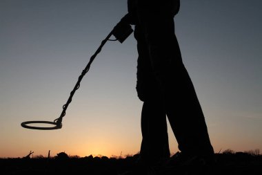 Batan güneşin arka planında mayın dedektörü olan bir adamın silueti.