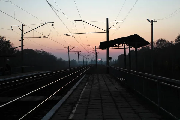 A platform and two tracks of railroad tracks, receding towards sunset.