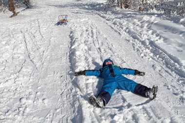 Oğlan kollarını açmış karda yatıyor.