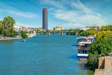 Seville 'deki Guadalquivir nehri boyunca, Gerçek Parroquia de Senora Santa Ana' nın çan kulesiyle renkli bir manzara. Endülüs, İspanya.