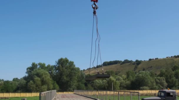 An einem Sommertag erhebt sich der grüne Teil der Brücke vorsichtig und bewegt langsam den roten Haken eines Baukrans durch die Baustelle — Stockvideo