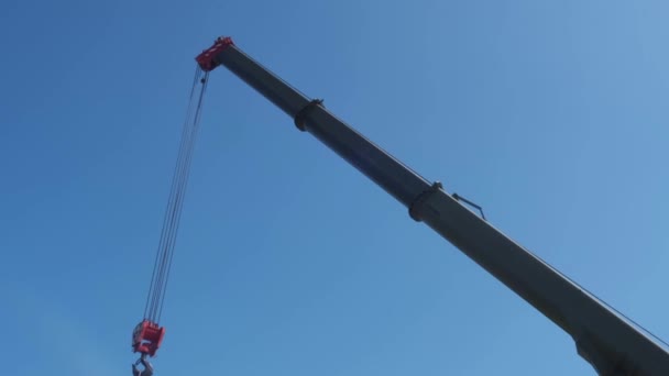 El gancho rojo de una grúa de construcción colgando de una pluma en un cielo despejado — Vídeos de Stock