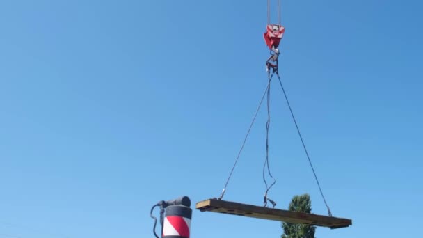 En un día de verano, la parte verde del puente se eleva con cuidado y lentamente se mueve gancho rojo de una grúa de construcción a través del sitio de construcción — Vídeo de stock