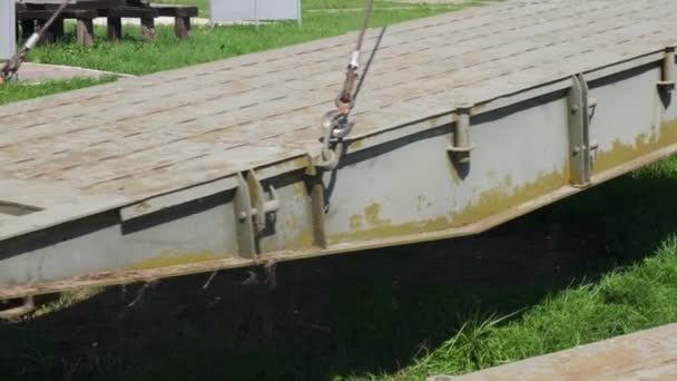 En un día de verano, la parte verde del puente se eleva con cuidado y lentamente se mueve gancho rojo de una grúa de construcción a través del sitio de construcción — Vídeo de stock