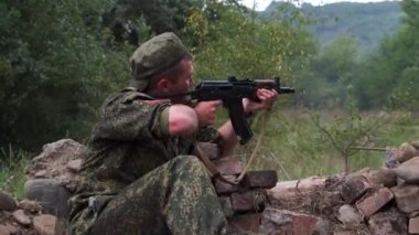 Rusya, Maykop - 2 Ağustos 2019. Bir asker siperde oturuyor, Ak-74 askeri silahlarının düşmanlarına ateş ediyor. Ormanda bir düşman askeri ile savaşmak. Duman ekranı
