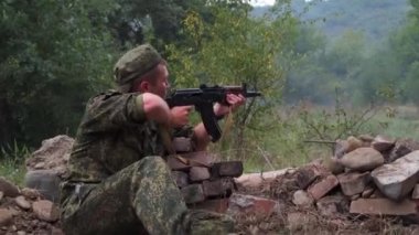 Rusya, Maykop - 2 Ağustos 2019. Bir asker siperde oturuyor, Ak-74 askeri silahlarının düşmanlarına ateş ediyor. Ormanda bir düşman askeri ile savaşmak. Duman ekranı