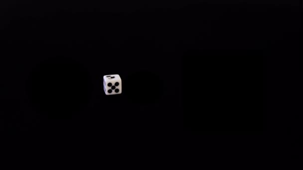 One playing white dice flies out on a black background. The cube flies, rotates on a black surface. Stops in sight. Concept of business and casino or gambling. Close-up. — Stock Video