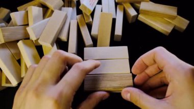 İnsan eli ahşap parmaklıklardan bir kule toplar. Oyun ahşap bir kule. Jenga oynarken blokların kulesi. Tahta bulmaca blokları. Tower block oyunu toplanıyor. Siyah arkaplan.