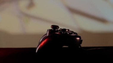 Oyun konsolunda video oyunu oynamak için masadaki siyah denetleyiciyi kapat. Büyük ekranın, projektörün ya da televizyonun önündeki oyun platformu. Işık mavi, kırmızı, yeşil.