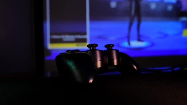黑色控制器在游戏控制台上玩电子游戏 在大屏幕 放映机或电视机前的Gamepad 相机沿着桌子移动 全景场景特写 浅色改为蓝色 — 图库视频影像