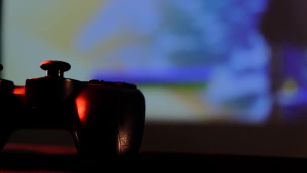 Vue rapprochée contrôleur noir sur table pour jouer à des jeux vidéo sur console de jeu. Gamepad devant un grand écran, un projecteur ou un téléviseur. Changement de lampe de lumière en bleu, rouge, vert . — Video