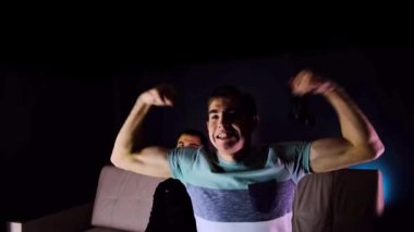 Zaferin tadını çıkarıyorum. Duygusal iki genç adam kanepede oturup oyun konsolu oynayıp, elinde joystick tutarak heyecanlılar. Kablosuz kontrolörle oyun oynayan erkekler. Samimi oda