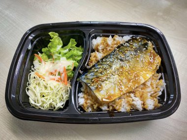 Plastik kaptaki pirinç kasesinin üstünde teriyaki sosuyla kızartılmış Saba balığı.