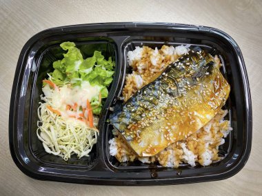 Plastik kaptaki pirinç kasesinin üstünde teriyaki sosuyla kızartılmış Saba balığı.