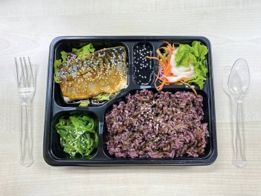 Plastik kaptaki pirinç kasesinin üstünde teriyaki sosuyla kızartılmış Saba balığı.