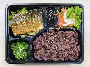 Plastik kaptaki pirinç kasesinin üstünde teriyaki sosuyla kızartılmış Saba balığı.