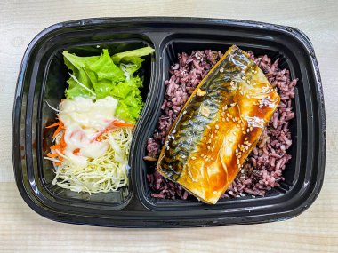 Plastik kaptaki pirinç kasesinin üstünde teriyaki sosuyla kızartılmış Saba balığı.