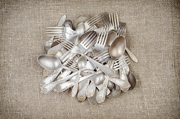 Pile of aged vintage silver cutlery on jute background — Stock fotografie