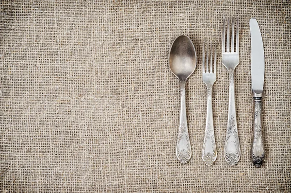 Leeftijd vintage zilveren vork, mes, lepel op jute-achtergrond — Stockfoto