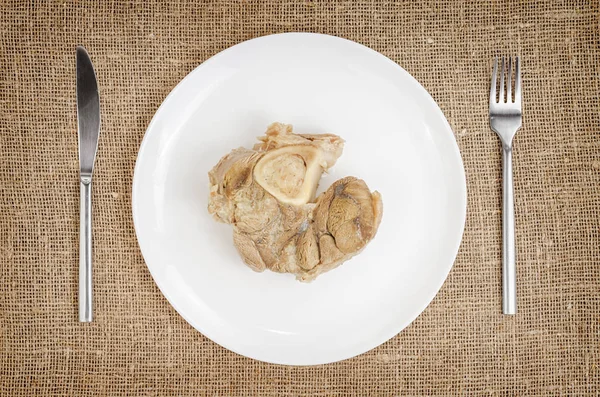 Leinenhintergrund mit gekochtem Schweinefleisch auf Teller mit Messer und Gabel — Stockfoto