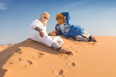 Sahara, Fas, 02-Ocak-2020. Bedevilerin portresi renkli türbanlı popüler Merzouga çölünde kum tepeciğinde oturuyor. Geleneksel kıyafetleriyle Tuareg 'li adam.