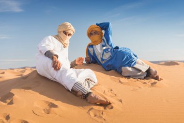 Sahara, Fas, 02-Ocak-2020. Bedevilerin portresi renkli türbanlı popüler Merzouga çölünde kum tepeciğinde oturuyor. Geleneksel kıyafetleriyle Tuareg 'li adam.