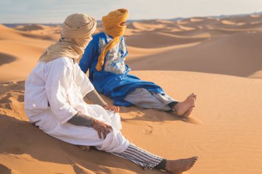 Sahara, Fas, 02-Ocak-2020. Bedevilerin portresi renkli türbanlı popüler Merzouga çölünde kum tepeciğinde oturuyor. Geleneksel kıyafetleriyle Tuareg 'li adam.