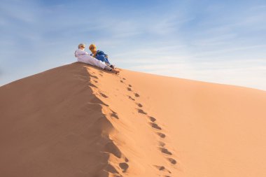 Sahara, Fas, 02-Ocak-2020. Bedevilerin portresi renkli türbanlı popüler Merzouga çölünde kum tepeciğinde oturuyor. Geleneksel kıyafetleriyle Tuareg 'li adam.