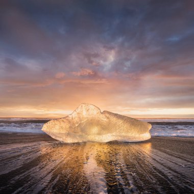 İzlanda 'nın ünlü Diamond plajında güzel bir gün batımı. Bu kum lav plajı, İzlanda 'nın güneydoğusundaki siyah kum plajlı buzul gölü Jokulsarlon Buz Kayası' nın yakınına yerleştirilmiş birçok dev buz mücevheriyle doludur.