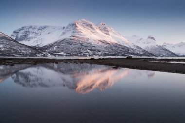 Karlı fiyortların ve dağ sırasının panoraması, Senja, Norveç İnanılmaz Norveç deniz manzarası popüler turistik cazibe merkezi. En ünlü seyahat yerleri. Muhteşem kış manzarası içinde güzel bir gün batımı