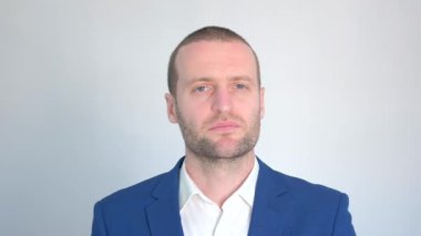 Mavi iş ceketli genç işadamı beyaz arka plandaki kameraya bakıyor.