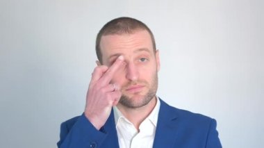 Mavi iş ceketli genç işadamı beyaz arka plandaki kameraya bakıyor.