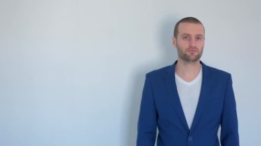 Mavi iş ceketli genç işadamı beyaz arka plandaki kameraya bakıyor.