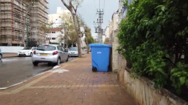ISRAEL - Netanya, 19 Mart 2020: Mavi pastik çöp kutusu veya kutu ve caddede bank