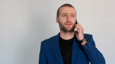 Mavi ceketli genç yakışıklı iş adamı kameraya bakıyor ve telefonla konuşuyor.