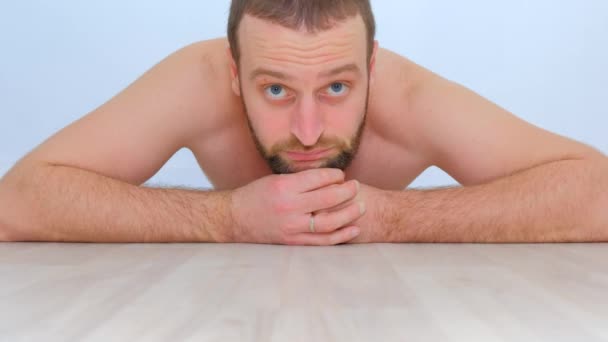 青い目と裸の胴を持つ若いハンサムな男が床に横たわってカメラを見て — ストック動画
