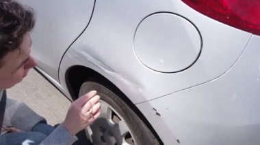 Yakışıklı genç bir kadın, bir trafik kazasından sonra arabasının arka kanadında büyük bir çiziği inceliyor.