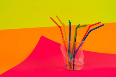 Çok renkli arka planda renkli pipetleri olan tek kullanımlık buruşmuş plastik bardak. Çöp ve Çevre Kirliliği kavramı.