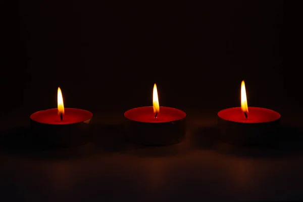 Three small pink wax decorative candles burn on a dark background. — ストック写真