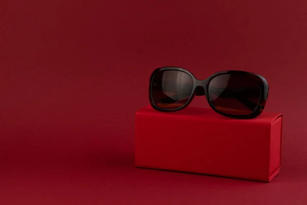 Kırmızı arka plandaki bir kutuda modaya uygun güneş gözlüğü. Asgari düzeyde. Minimalist moda fotoğrafı. — Stok fotoğraf