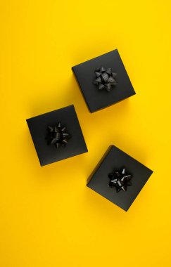 Sarı arka planda fiyonklu siyah hediye kutuları.